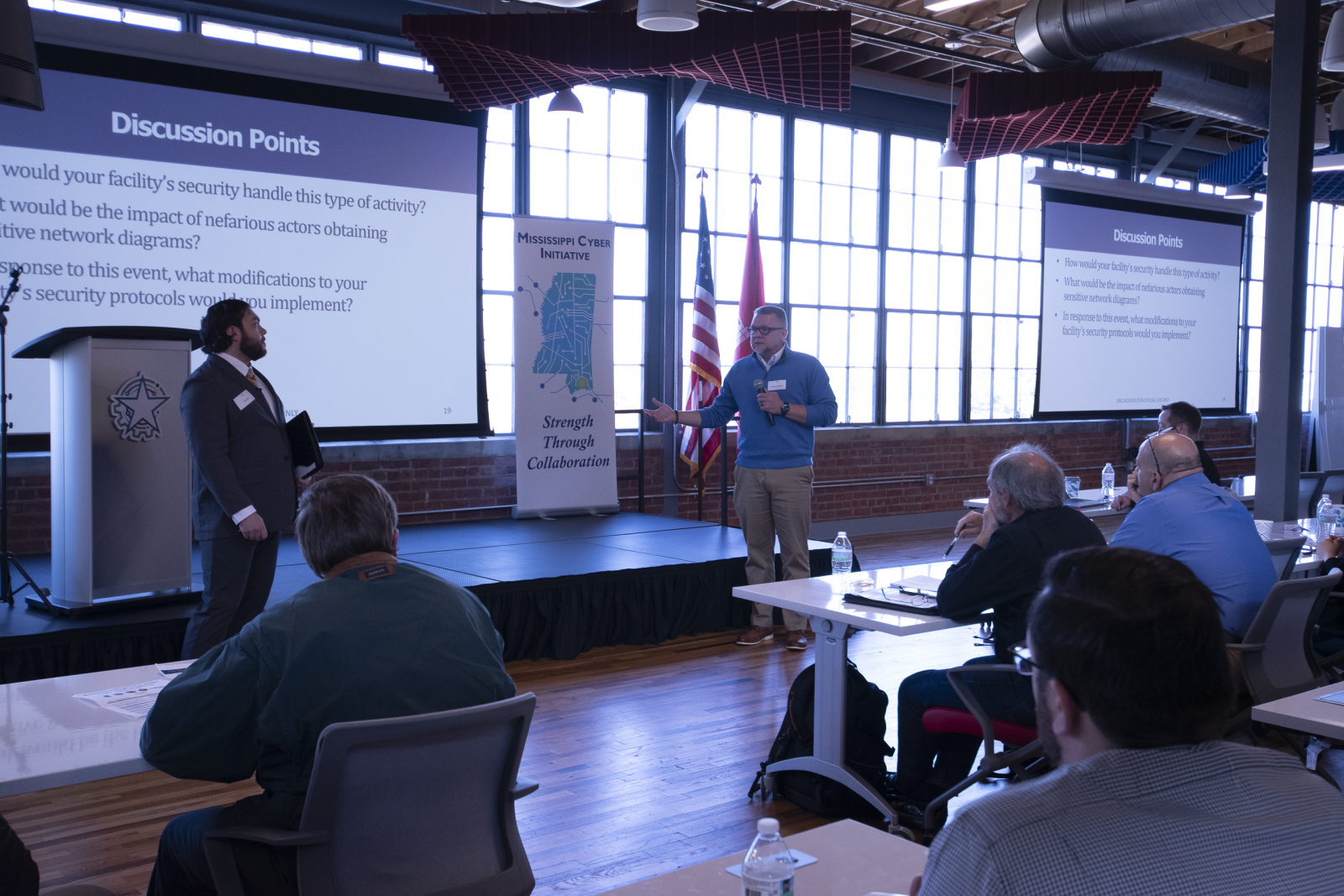Individuals speak in front of a group at MCI's Cyber Tabletop Exercise